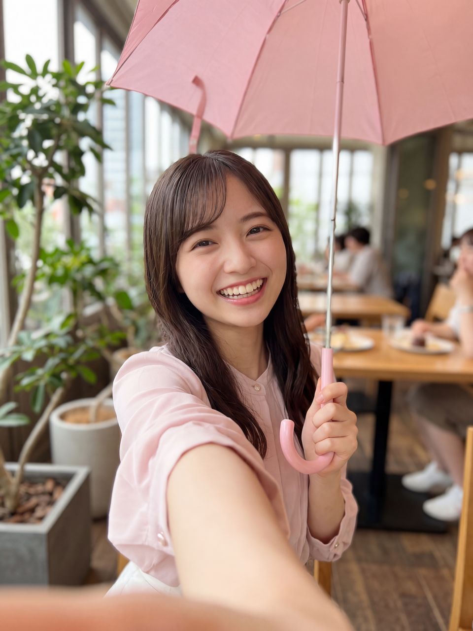さくら色の傘を持ってカフェのテラスで自撮りするさくら