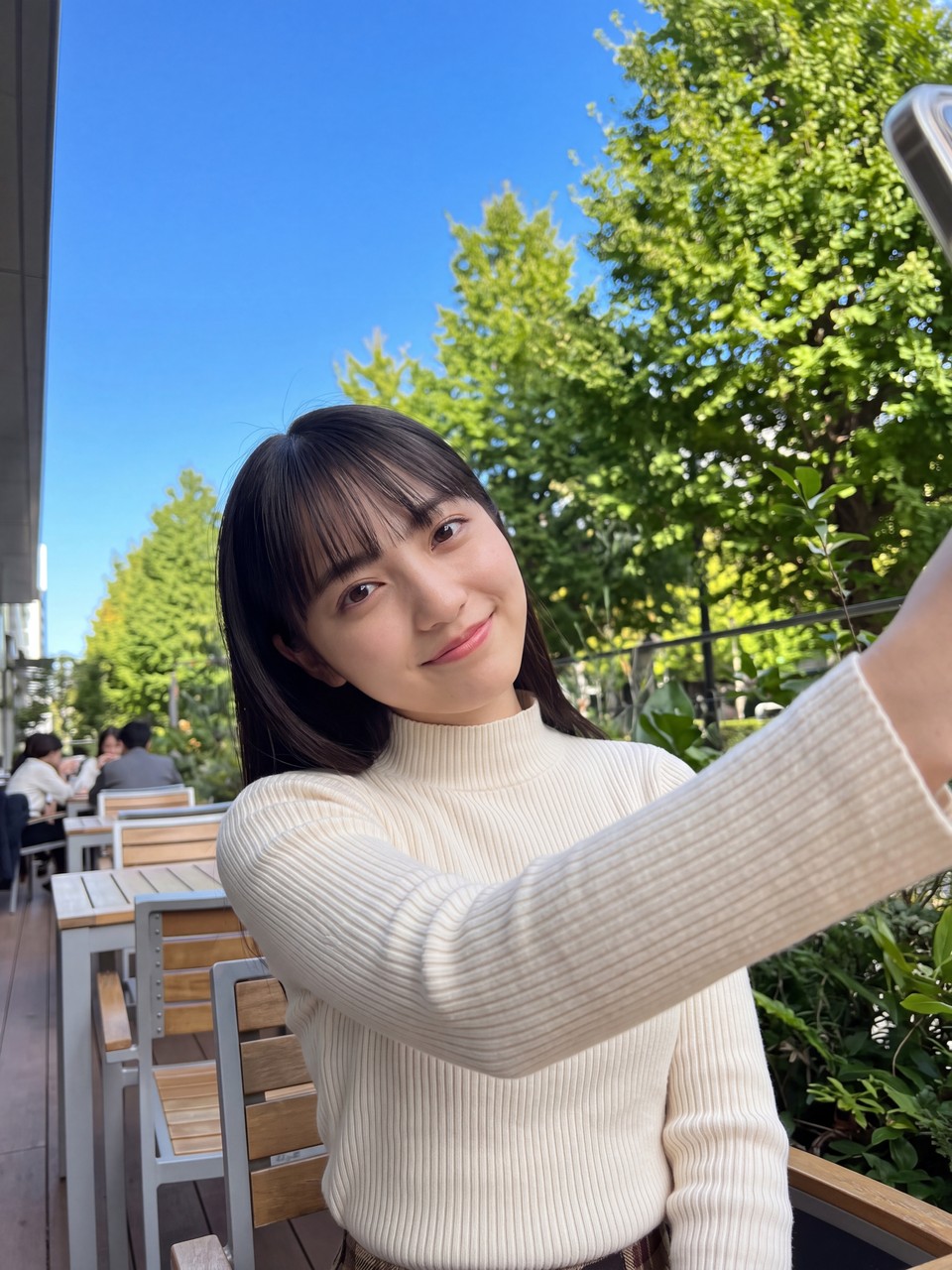 初秋の爽やかな光と緑に包まれたテラス席で優しくカメラを見つめ微笑む如月玲奈のエレガントな自撮りショット