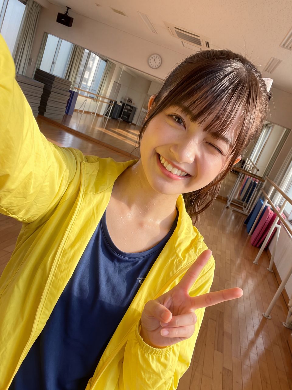ダンス練習スタジオで黄色いウインドブレーカーを着て特大ウインクと元気なピースサインを決める瀬戸朝陽の自撮りセルフィー