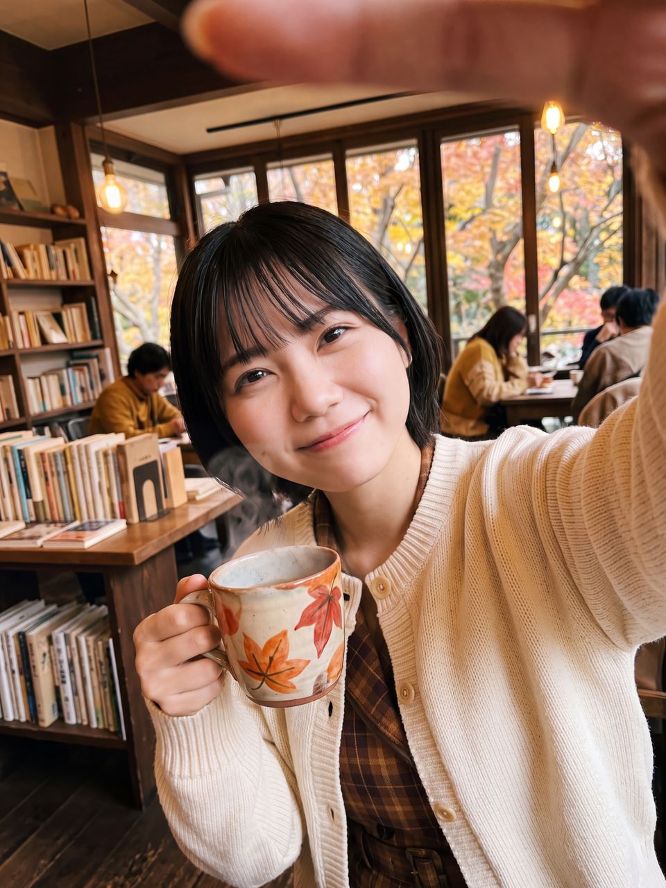 秋のブックカフェで紅葉柄のマグカップを手に穏やかな笑顔で見つめる天音かなでの自撮りショット