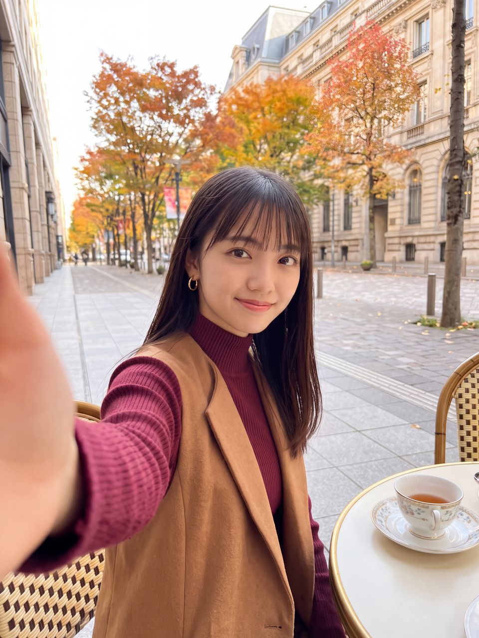 クラシカルなカフェテラス席で美しく色づく紅葉と街並みを背景に上品なティーカップを前に優しく微笑む如月玲奈の自撮りショット